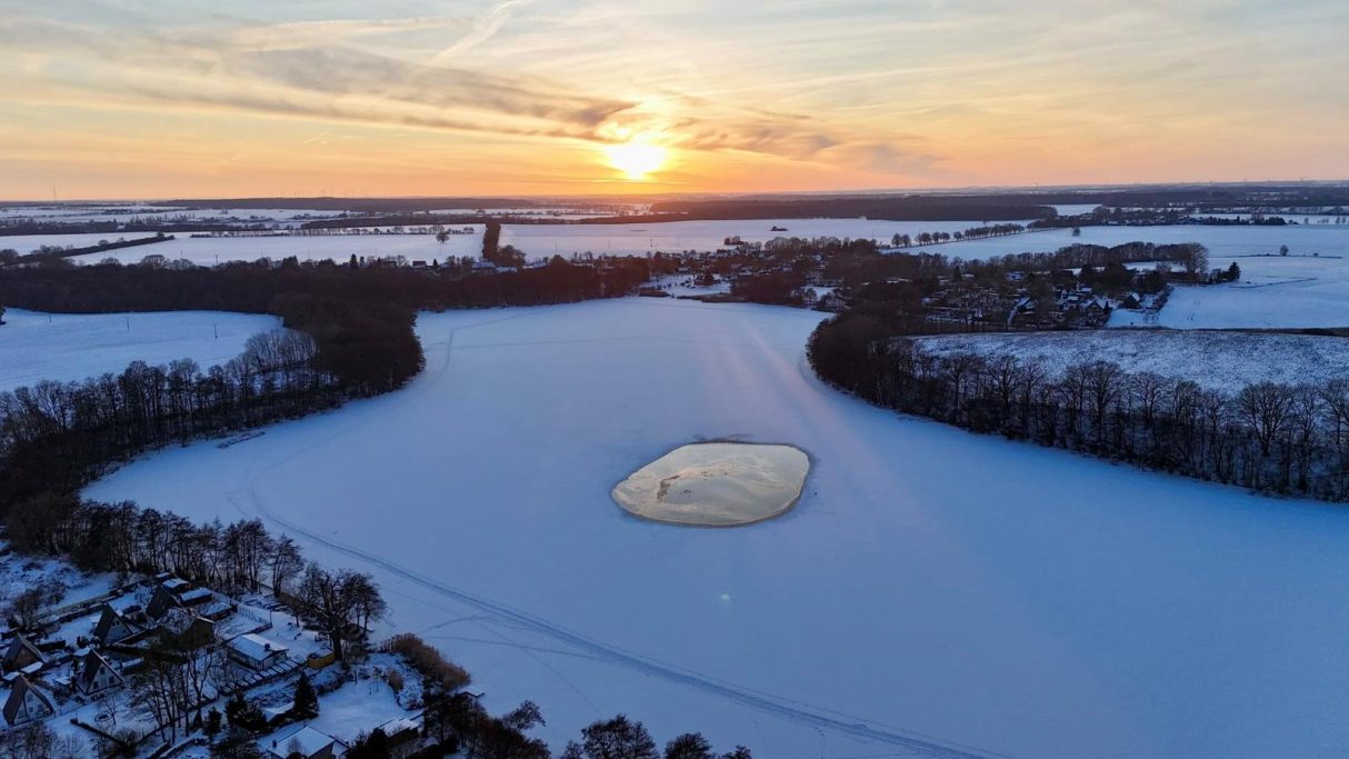 Winter auf dem Cramoner See Winterlandschaft mit einem gefrorenen See und Sonnenuntergang über einer schneebedeckten Ebene.
