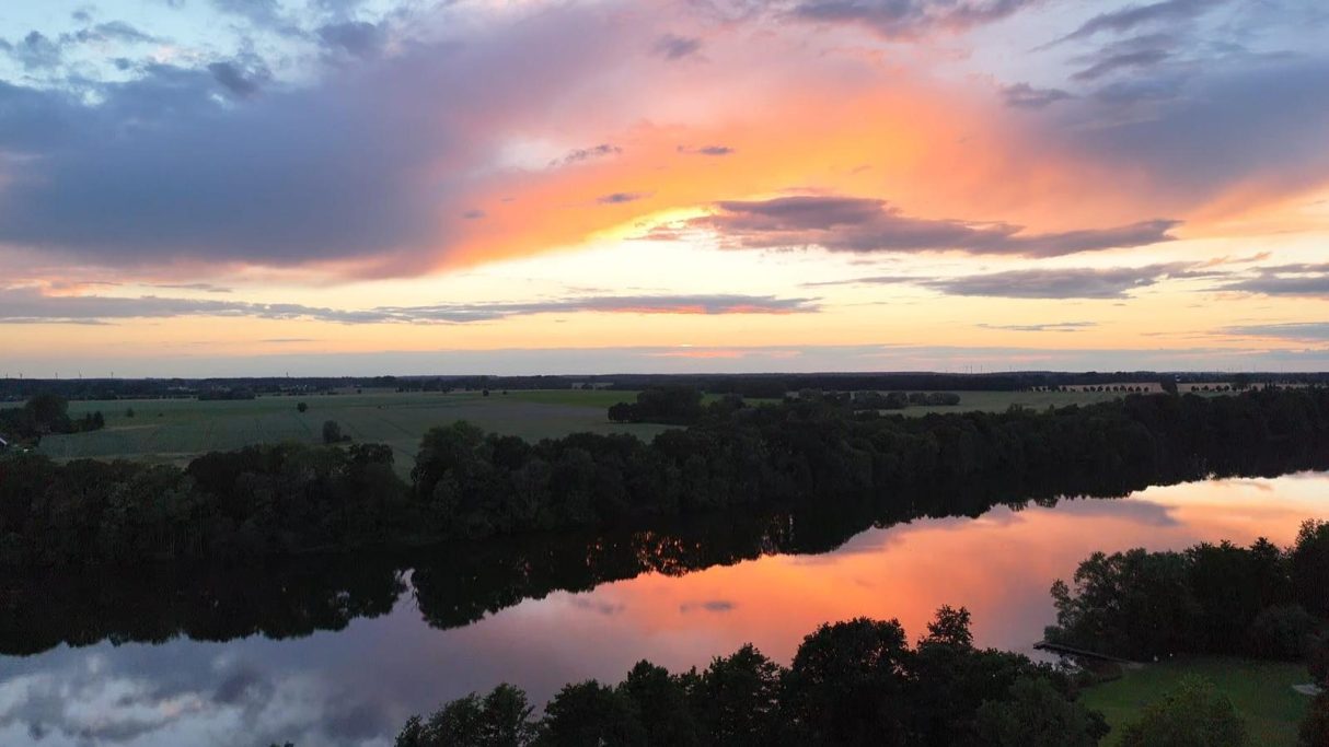 Abendstimmung am Cramoner See Sonnenuntergang über einem ruhigen Fluss, umgeben von Wäldern und Wiesen.